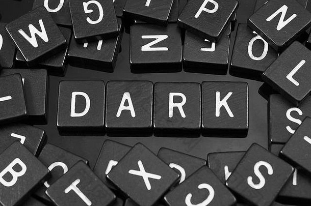 黑色字母瓷砖，在反光背景上拼写单词“暗”