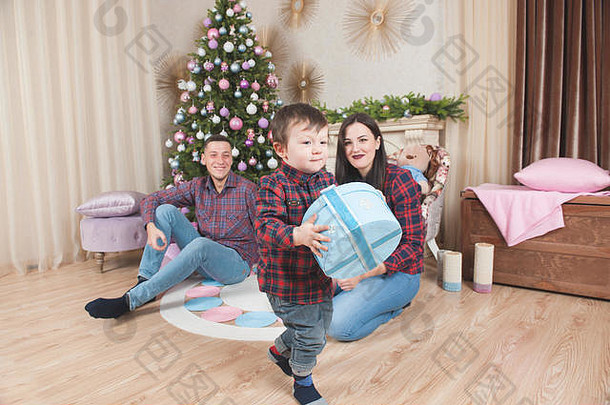 小男孩拿着圣诞礼物盒走在父母旁边，树上放着玩具