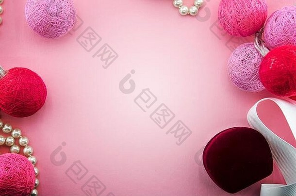 粉色背景配粉色和红色纱线或线球花环、白丝带、珠宝盒、珍珠项链。点燃棉线球。情人