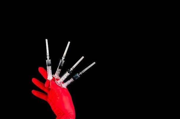 戴着红色橡胶手套的手在黑色背景上拿着几个注射器。空间。疫苗接种的概念。