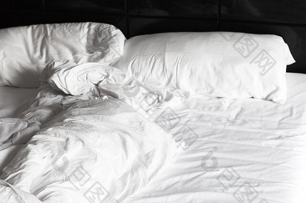 皱巴巴的毯子和枕头躺在一张空床上，睡觉时间背景照片