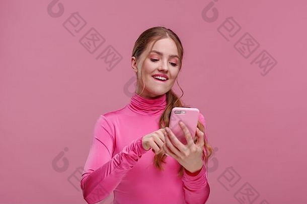 有史以来最好的一天。这位年轻的红发女子手持粉色智能手机，面带微笑，表现出积极的态度。快乐女孩得到了令人震惊的好消息。警察