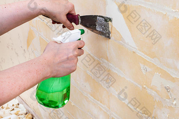 装修房间：准备墙壁。用金属抹刀从湿旧墙纸上清洁墙壁
