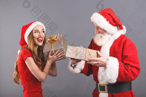 圣诞老人老人白色胡子穿sungasses年轻的夫人老人穿圣诞老人他红色的衣服太阳镜站灰色的背景兴奋夫人圣诞老人摇礼物银包装笑圣诞老人老人一年圣诞节假期记忆礼物购物折扣商店雪少女圣诞老人老人化妆发型狂欢