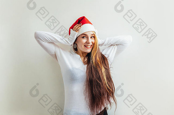 戴着红色圣诞老人帽、留着长发的美丽女孩，被隔离在白色背景上，看上去快乐而兴奋。年轻女子肖像，真实情感。圣诞快乐，新年快乐。