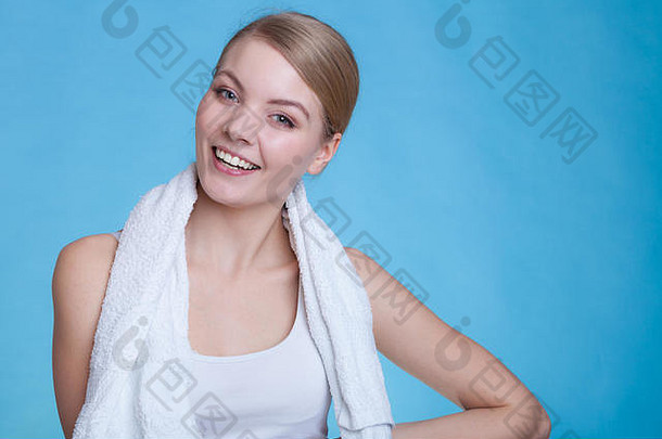 锻炼，卫生概念。一个微笑的女人，肩上挎着一条毛巾，对着摄像机微笑，摄影棚在蓝色背景下拍摄