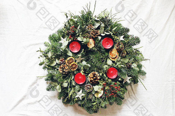 白色桌子背景上的圣诞花环。由常绿冷杉树枝、桉树叶子、木星、松果、浆果和红蜡烛装饰而成。平面布置，俯视图。