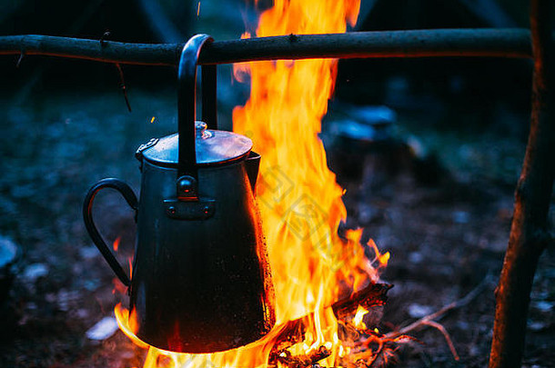 古老的复古铁制露营壶在森林里的火上<strong>烧开</strong>水。明亮的火焰，黄昏的篝火。