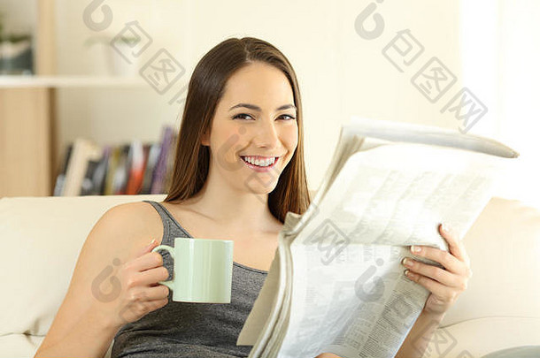 家里客厅里，一个快乐的女人拿着报纸和咖啡杯，坐在<strong>沙发</strong>上看着摄像机