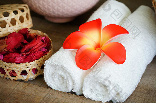 白色毛巾在水疗桌上的干玫瑰香旁用橙色花朵装饰。