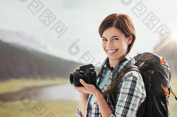 年轻的微笑女摄影师拍摄在户外自然徒步旅行山持有数字相机
