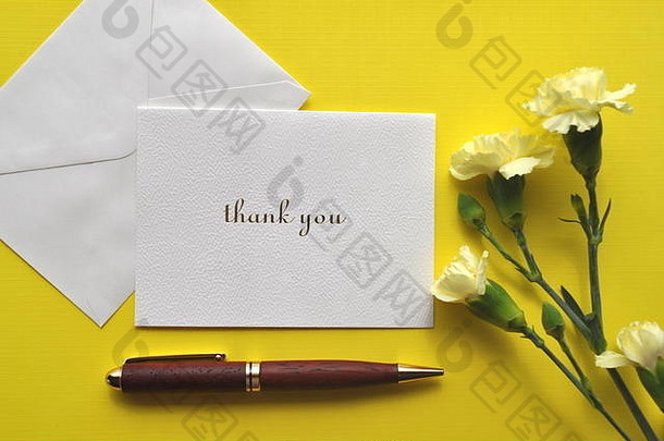 一张白色的感谢卡，在明亮的黄色背景上有钢笔和花。有复印空间的平板。