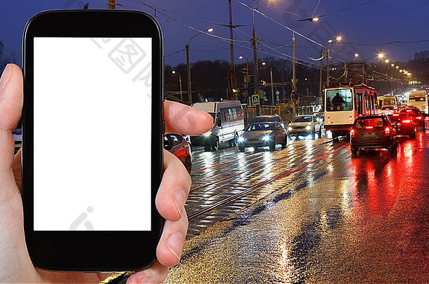 旅游理念-手持智能手机，屏幕镂空，背景为夜间潮湿的城市街道