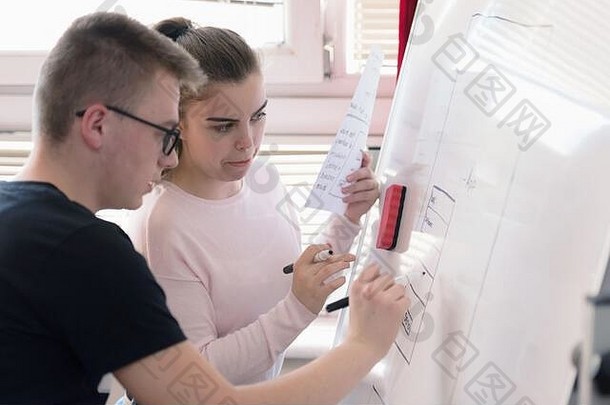 两个年轻的大学生上课时在黑板上写字。解决<strong>数学</strong>问题或提出解决问题的想法。