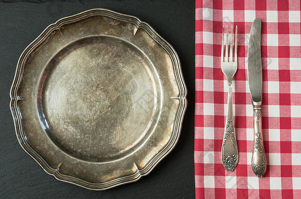空的金属盘子，板岩背景上有刀叉，并留有空间供您选择菜单或菜谱。餐馆的菜单卡。桌板设置。