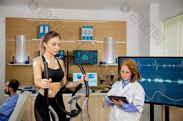 女运动员在踏步机上进行测试，医生在平板电脑上做笔记。电极试验