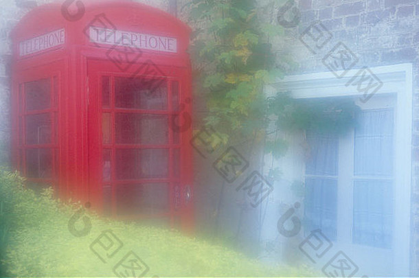 大气的老式英国红色电话亭挤在树篱和石砖房子之间的一个角落里