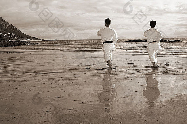 阳光明媚的日子里，带着黑带的年轻成年男子在海滩上练习卡塔舞