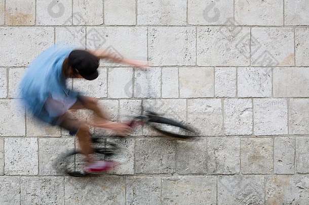 城市里年轻的骑自行车的人在墙上骑自行车跳来跳去。灰色和蓝色的<strong>创意壁纸</strong>背景照片。静态和动态背景