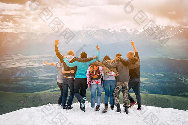 一群朋友很高兴爬上了山顶。他们拥抱和跳跃。背着相机看远处。