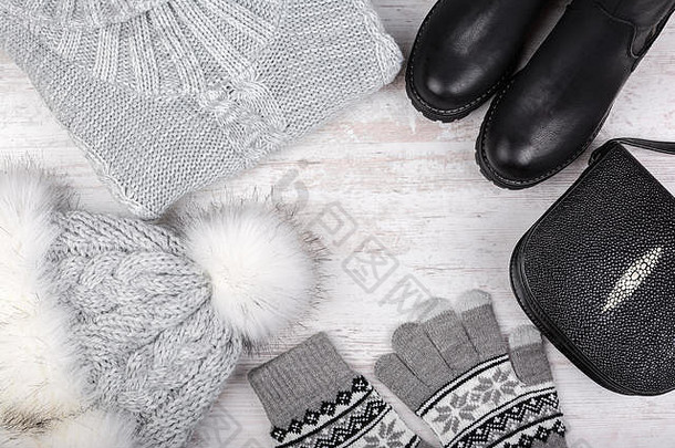 一套时尚的冬季女装。白色木质背景上的羊毛衫、鞋子、手提包、皮帽和手套。