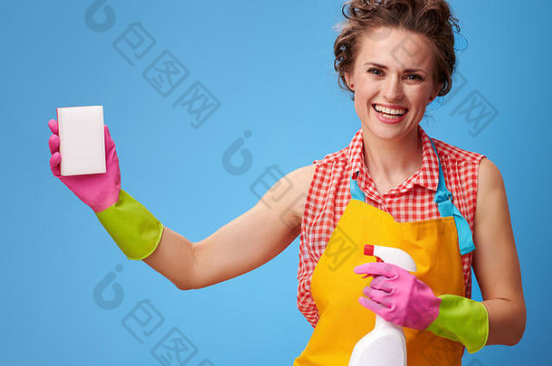 大扫除时间。快乐的现代家庭主妇，带着橡胶手套和清洁剂，在蓝色背景下使用厨房海绵