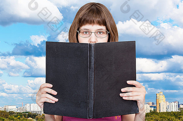 戴眼镜的女孩读着一本大书，<strong>书的封面</strong>是空白的，背景是城市上空的蓝天