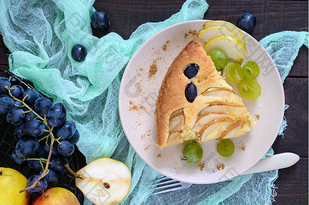 一大块馅饼，在深色木制背景上的盘子上放着梨和葡萄。