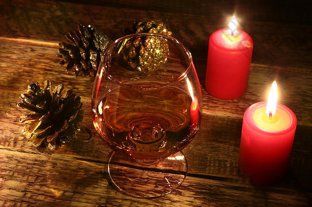 圣诞蜡烛和玻璃，木质背景上有白兰地或威士忌。圣诞装饰。