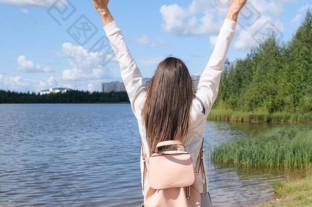 张开双手的女孩。自然的自由。一个女孩站在那里享受着美丽的阳光。一个女孩站在露天的水边。年轻女子