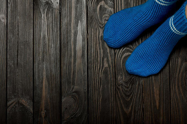 腿部编织蓝色羊毛袜，木质深色背景。