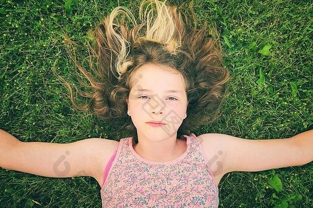 11岁的女孩躺在草地上，双臂张开，脸上表情严肃