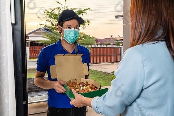 送货员在家给顾客送比萨食品时，人们必须戴口罩以防止冠状病毒（新冠病毒-19）的传播