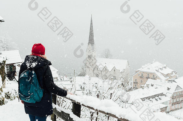 奥地利暴风雪期间，一位戴着红帽子的妇女正在欣赏哈尔斯塔特古城的景色。