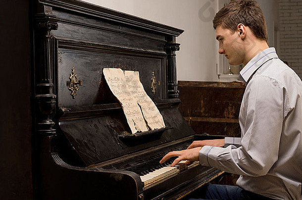 一个年轻人在钢琴前练习<strong>朗诵</strong>，从一张破烂的乐谱看乐谱，侧视图
