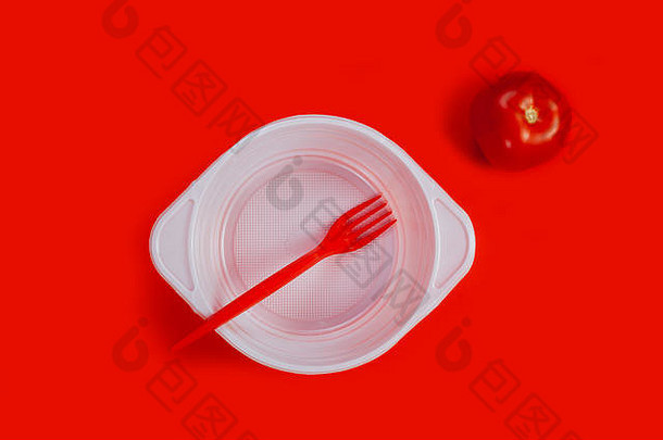 白色塑料盘，番茄和红色叉子，红色背景。
