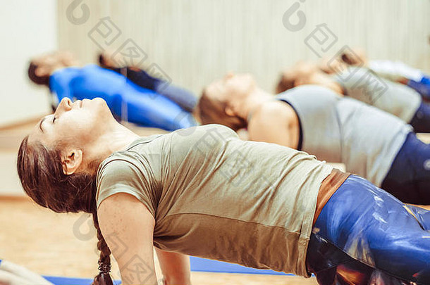穿着运动服的漂亮女孩正在体育馆的瑜伽垫上做瑜伽