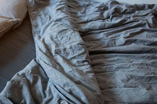 一张灰色的棉布床单，床上有枕头的毯子