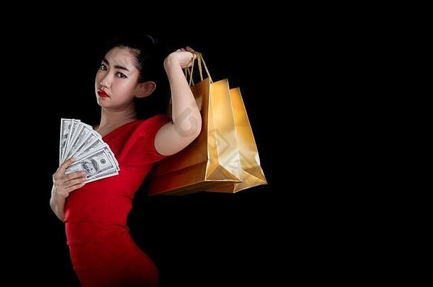 一位身穿红色连衣裙、手持和购物袋、背景为黑色的美丽亚洲年轻女子的肖像，销售理念，请看