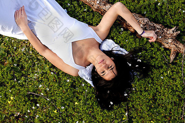 在杏树旁的绿色草地上，一位穿着白色连衣裙的美丽女孩的照片