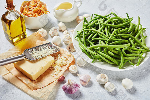 在混凝土桌上的白色盘子上放着豆荚状的新鲜绿豆，罐子里装着香酥的法式炸洋葱圈、奶酪、蘑菇和新鲜奶油