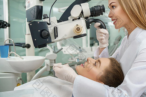 做牙医<strong>的</strong>漂亮女人，检查病人<strong>的</strong>牙齿。专业口腔医生通过现代牙科显微镜观察，手持器械。病人躺在牙医椅上。