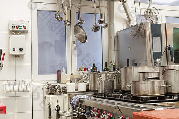 商业厨房内部整洁，壁挂式餐具，中央燃气灶上有一系列不同的不锈钢锅