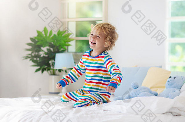 孩子们在有窗户的阳光明媚的白色卧室里的床上玩耍。儿童房和室内设计。小男孩在家。儿童托儿所用床上用品和纺织品。碘化钾