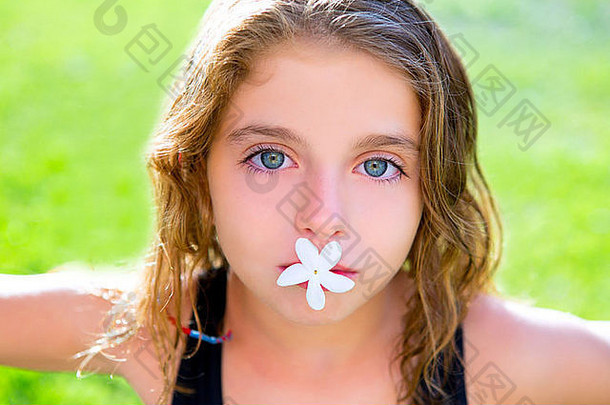 蓝眼睛的小女孩嘴里叼着茉莉花在花园的草地上