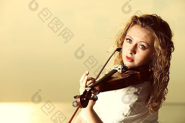 日落或日出时，金发碧眼的音乐爱好者在码头上拉着小提琴。热爱音乐的理念。