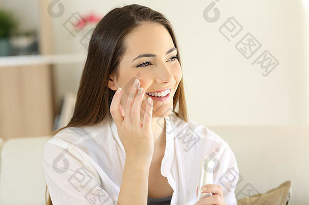 一位美女坐在家客厅的沙发上，在脸上涂保湿霜