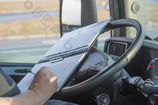 卡车司机手的特写视图，该司机正在文档中书写。照片拍摄于驾驶室。