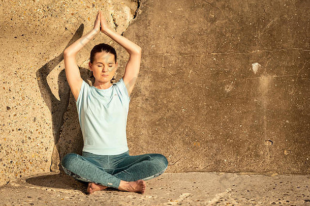 在水泥墙边练习瑜伽和在阳光下冥想的女人