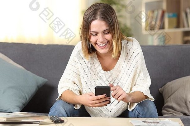 一个快乐的<strong>女</strong>孩坐在家客厅的沙发上用手机拍摄的正面照片